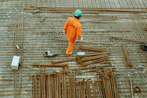 A construction worker in a green helmet and orange jumpsuit works on the worksite.